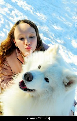 Une adolescente joue avec un chien de la race Samoyed blanc neige et grand elle joue à l'extérieur Banque D'Images