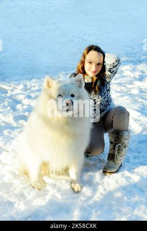 Une adolescente joue avec un chien de la race Samoyed blanc neige et grand elle joue à l'extérieur Banque D'Images