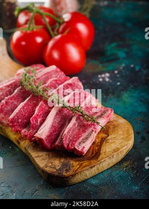 Sur une planche à découper en bois, des morceaux de viande crue avec une branche de romarin, appétissant des tomates mûres sur un fond de marbre turquoise. Recettes de cuisine
