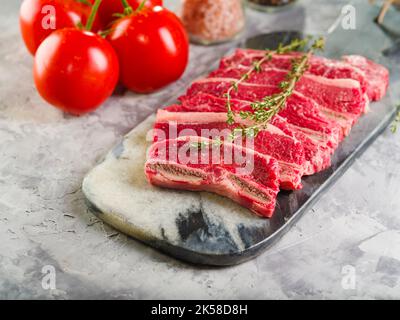 Gros plan. Steaks de viande crus avec une branche de romarin sur une planche à découper, tomates mûres et épices sur un fond clair. Restaurant et cuisine maison REC Banque D'Images