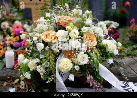 fleurs funéraires pastel sur une tombe devant une croix en bois sur fond flou Banque D'Images