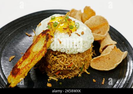 Spécialité alimentaire asiatique Nasi goreng, littéralement riz frit en indonésien, servir avec du poulet, des œufs, de la sauce aux arachides et des crevettes Banque D'Images