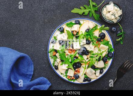 Delicious arugula salad with pears, blueberries, roquefort cheese and walnuts. Black kitchen table background, top view Banque D'Images
