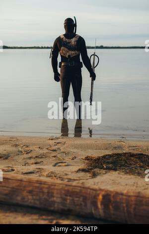 Vue arrière d'un plongeur dans une combinaison tenant un fer de lance. Un jeune homme aventureux se prépare à aller pêcher dans l'eau de mer. Banque D'Images