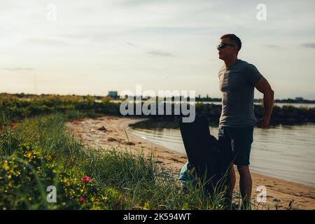 Un plongeur qui se défait de sa chemise tout en se tenant debout avec son équipement de plongée à la plage. Jeune homme aventureux se préparant à entrer dans l'eau par lui-même Banque D'Images