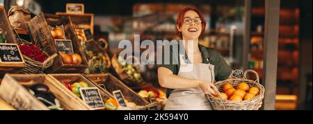 Le grand propriétaire d'une épicerie qui a réussi à sourire à l'appareil photo tout en tenant un panier de fruits de raisin frais biologiques. Bonne femme entrepreneur à la course d'un petit bu Banque D'Images