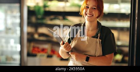 Un jeune propriétaire de boutique souriant à la caméra tout en tenant une tablette numérique. Joyeuse entrepreneur de la gestion d'une petite entreprise réussie dans le f Banque D'Images