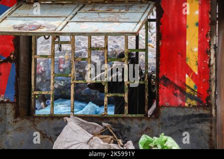 Kisumu, Kenya. 04th octobre 2022. Un préparateur de déchets qui a livré des bouteilles en plastique pour recyclage est vu à travers les grilles métalliques d'une fenêtre dans un centre de collecte en plastique à Kisumu. Des militants et des groupes environnementaux au Kenya et dans d'autres parties du monde ont dénoncé la société Coca-Cola qui serait nommée sponsor du sommet climatique de cette année, la CdP 27, qui se tiendra en novembre en Egypte. Crédit : SOPA Images Limited/Alamy Live News Banque D'Images