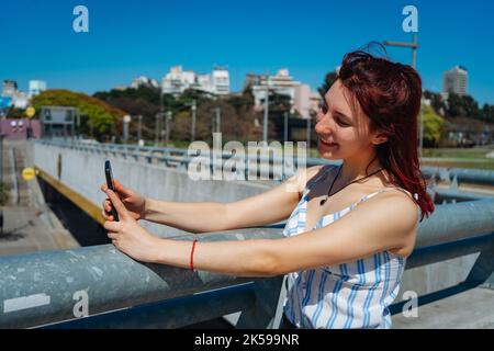 Une jeune femme aux cheveux rouges prend un selfie avec son téléphone cellulaire. Copier l'espace. Orientation paysage. Banque D'Images