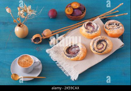 Mini-chaussons remplis de graines de pavot moulues avec des prunes fraîches sur une table en bois bleu, angle de vue élevé, pas de personnes. Banque D'Images