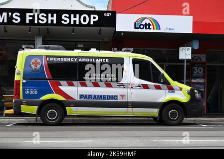 Vue latérale d'une ambulance d'urgence Ambulance Victoria garée sur le côté d'une route dans une rue commerçante, avec des boutiques en arrière-plan Banque D'Images