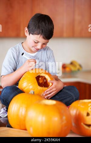 Mon Jack-O-Lantern va être le meilleur. Un petit garçon assis à pattes croisées et dessinant un visage sur une lanterne Jack. Banque D'Images