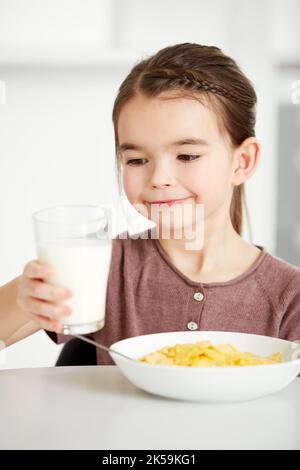 C'est une bonne façon de commencer la journée. Une petite fille mignonne boit un verre de lait avec ses céréales. Banque D'Images