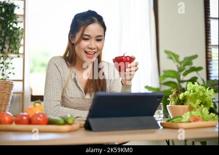 Jolie et charmante jeune femme asiatique blogueuse de nourriture ou nutritionniste en direct sur sa chaîne pour enseigner et parler avec ses disciples tout en cuisinant h Banque D'Images