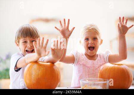 Ils aiment la sculpture de citrouille. Portrait d'un petit garçon et d'une fille regardant excitée tout en creusant leur Jack-o-lanterne. Banque D'Images