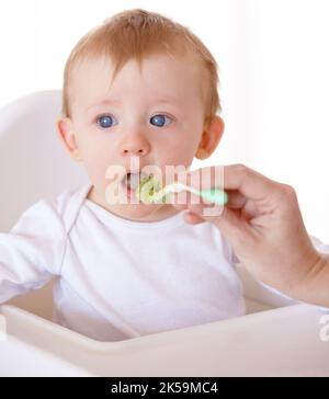 Essayons. Un bébé mignon recevant une cuillerée de nourriture de sa mère. Banque D'Images