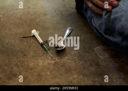 Outils addicts. Gros plan d'une personne assise à côté d'une seringue et d'une cuillère à café utilisée dans la prise de drogues dures. Banque D'Images
