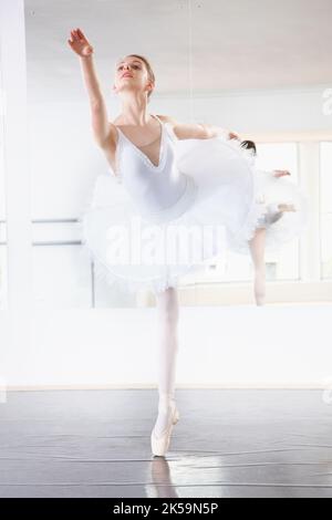 Ballerine statuesque. Prise de vue en longueur d'une répétition de ballerine dans un studio avec un miroir derrière elle. Banque D'Images