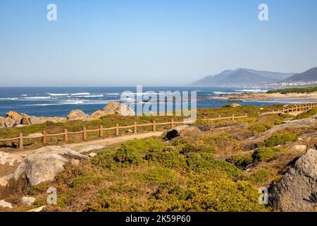 Passerelle avec clôture le long de la côte de l'océan Atlantique avec montagne en arrière-plan. Mousse et herbe sur les rochers en bord de mer. Large plage sur Camino de Santiago. Banque D'Images