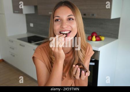 Belle femme saine et attrayante mangeant des fruits secs à la maison Banque D'Images
