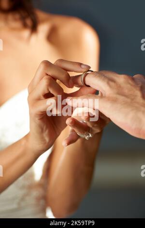 S'engager aux fidéliser. Vue rognée d'une mariée glissant un anneau sur son doigt de marié. Banque D'Images