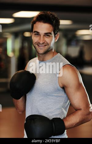 Prêt à l'emploi. Portrait d'un homme souriant portant des gants de boxe et des vêtements de sport se posant prêt à se battre à la salle de gym. Banque D'Images