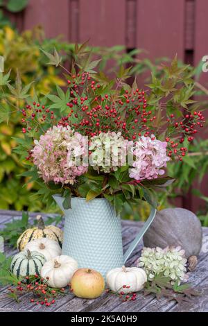 bouquet d'automne de fleurs d'hortensia, de hanches roses et de feuilles d'érable dans une carafe d'époque Banque D'Images