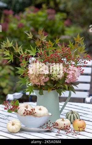 bouquet d'automne de fleurs d'hortensia, de hanches roses et de feuilles d'érable dans une carafe d'époque Banque D'Images