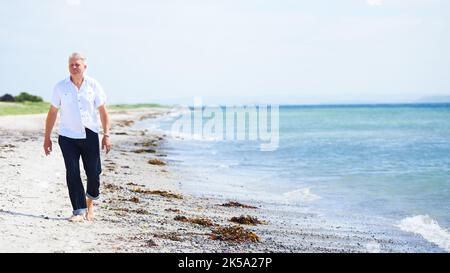 Admirez la beauté de l'océan. Un homme âgé marchant pieds nus sur le rivage. Banque D'Images