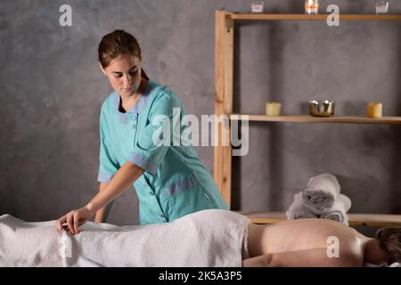Jeune belle femme sur une table de massage dans le spa de beauté. Masseuse se mettre au travail avec le patient. Banque D'Images