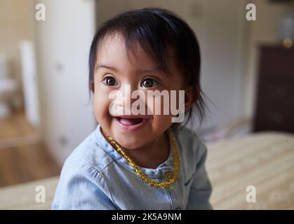 Bébé, fille et mignon avec un syndrome de Down petit enfant sur un lit dans la chambre de sa maison seule. Les enfants, les enfants et le visage avec un enfant doux de sexe féminin Banque D'Images