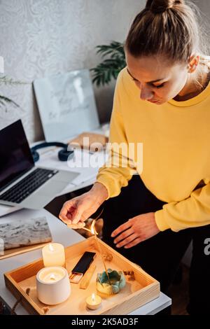 Méditation, relaxation après le travail. Femme se prépare à méditer et allume le bâton d'encens indien et les bougies. Femme mains avec la fumée indienne Banque D'Images