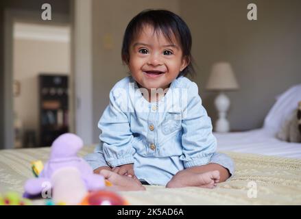 Syndrome de Down et portrait de bébé heureux sur le lit avec la joie des besoins spéciaux mexicains enfant détendu à la maison. Bonne petite fille au Mexique avec handicap et Banque D'Images