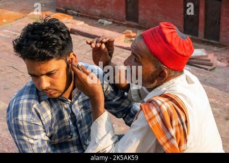 NEW DELHI - SEP 17: Travailleur de rue indien avec une aiguille nettoyant l'oreille d'une personne dans une rue à New Delhi, sur 17 septembre. 2022 en Inde. Banque D'Images