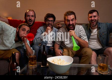 Un groupe d'amis masculins s'est réuni pour assister à un match de football, célébrant un score de but, criant joyeusement. Banque D'Images