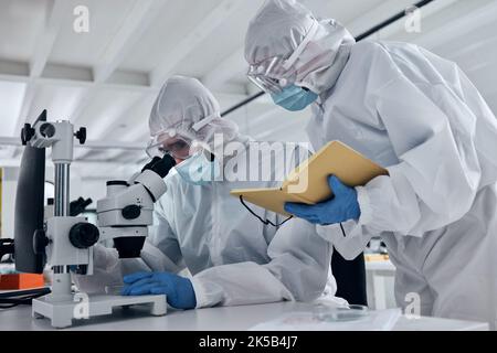 Équipe scientifique, recherche covid et microscope avec équipe écrivant des notes ou des résultats pendant l'analyse d'un échantillon dans un laboratoire scientifique et médical. Médical Banque D'Images