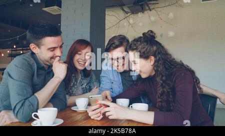 Les jeunes gens heureux regardent l'écran du smartphone discuter des photos et rire pendant la pause déjeuner dans le café. Amitié, technologie moderne et concept de style de vie moderne. Banque D'Images