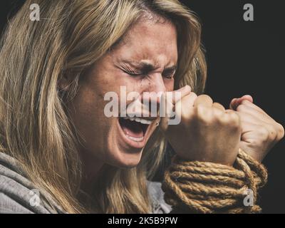 Danger, peur et horreur femme hurle pour l'aide avec les mains cravate et piégé par la corde sur fond noir studio. Violence, triste ou anxiété femme avec Banque D'Images