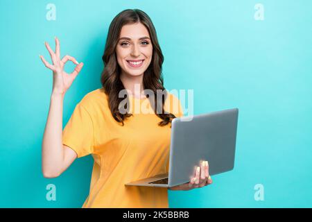 Gros plan photo de jeune professionnel toothy positive mignon fille porter un t-shirt orange montrant le signe d'âne tenir ordinateur portable programmeur isolé sur la couleur cyan Banque D'Images