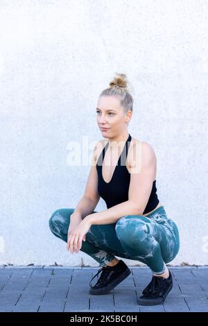 Portez une jeune fille sportive aux cheveux longs blonds dans un haut de sport noir et bleu et des leggings sont assis sur le sol. Photo de haute qualité Banque D'Images