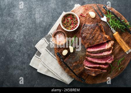 Steaks. Steak de viande grillé en tranches de New York ou de la striploine aux épices romarin et poivre sur un plateau en marbre noir sur fond gris pierre ancien. Vue de dessus. Banque D'Images