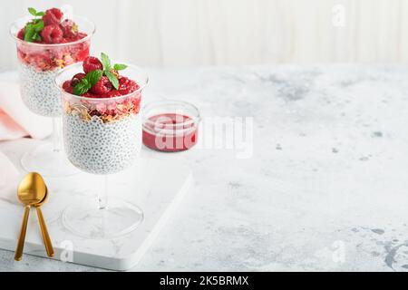 Pudding au Chia. Pudding sain au chia de vanille dans un verre avec des framboises fraîches et de la menthe sur fond blanc. Petit déjeuner sain végétalien. Banque D'Images