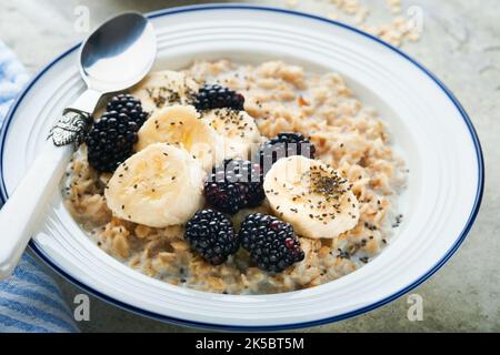 Flocons d'avoine. Bol de porridge de flocons d'avoine avec des graines de mûre, de banane et de chia sur fond de table vieux en béton gris. Vue de dessus en style de pose à plat. Naturel i Banque D'Images