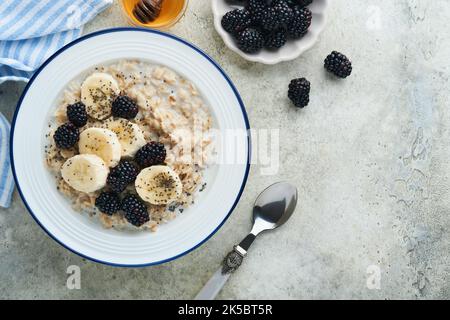 Flocons d'avoine. Bol de porridge de flocons d'avoine avec des graines de mûre, de banane et de chia sur fond de table vieux en béton gris. Vue de dessus en style de pose à plat. Naturel i Banque D'Images