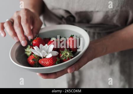 Une assiette de fraises en céramique grise dans les mains des femmes. Banque D'Images