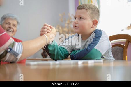 le garçon secoue les mains avec sa grand-mère. il est très concentré et sérieux. en arrière-plan se trouve sa grande-grand-mère, souriant et espérant qu'il le fera Banque D'Images