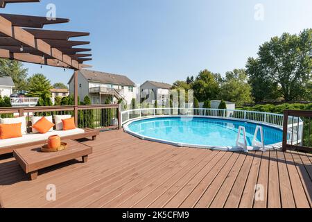 Une terrasse arrière avec une pergola sur quelques sièges et une grande piscine hors sol. Banque D'Images