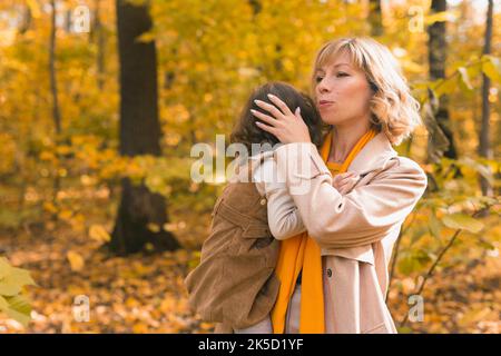 La mère apaise sa fille blonde qui pleure. Maman tient bébé de tristesse dans ses bras en nature d'automne. Banque D'Images