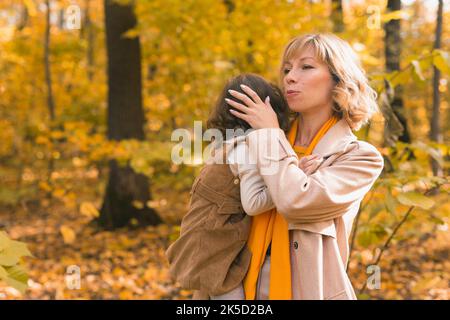 La mère apaise sa fille blonde qui pleure. Maman tient bébé de tristesse dans ses bras en nature d'automne. Banque D'Images