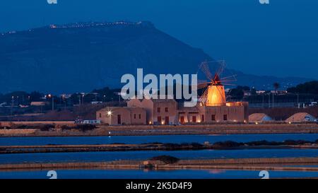 Italie, Sicile, Trapani, sel, bleu crépuscule, moulin avec dépendances comme sujet principal, le moulin à vent est illuminé jaune, dans le premier plan du bassin des travaux de sel traversé par des barrages, dans le fond s'élève les Mons Erix, sur lui l'Erice illuminé Banque D'Images